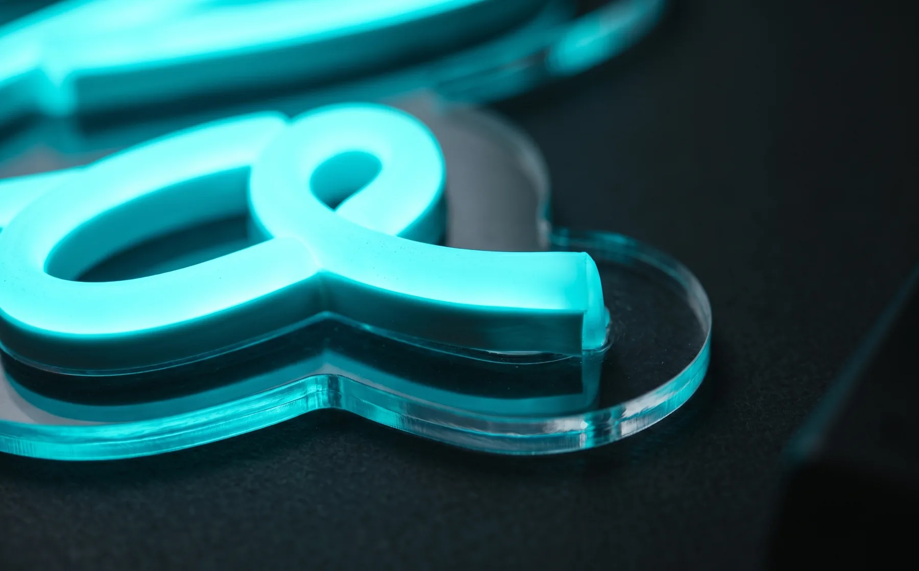 Macro close-up of a cyan LED neon tube mounted on a laser-cut clear acrylic backing, showing the smooth even glow and polished acrylic edge
